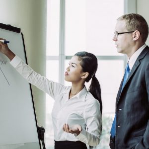 Young Asian business woman drawing growth diagram on flipchart for two partners. Business group analyzing sales forecast. Business meeting and analytics concept