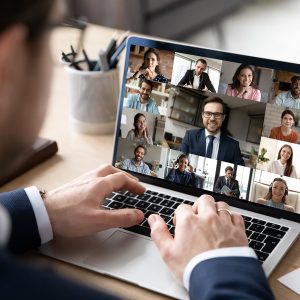 Close up rear view businessman engaged in online conference, using laptop, sitting at desk, diverse colleagues business people on computer screen, negotiations, briefing, employee making video call